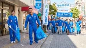 5月31日に南柏で行われる町会主導ゴミゼロ運動の告知バナーを掲げ、地域住民と共に青いツナギを着てゴミ拾い活動を行う様子。